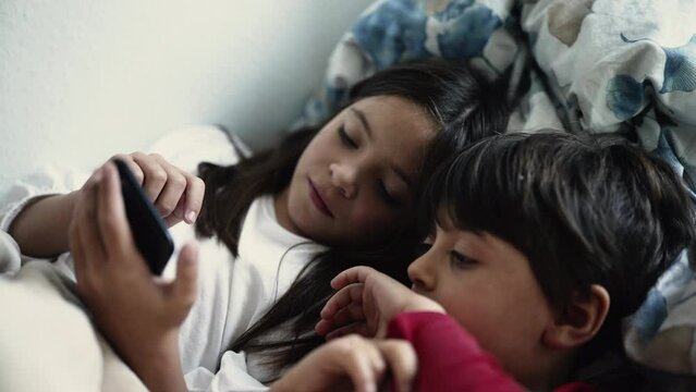 Brother and Sister Engrossed in Smartphone Screen While Lying in Bed, Siblings Bonding Over Digital Device