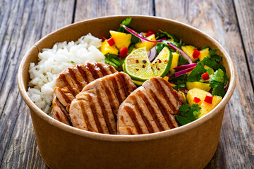 Grilled pork loin steaks with rice and mango salad in lunch box to go on wooden table
