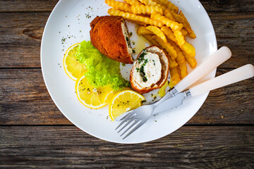 Cutlet de Volaille served with French fries and lemon on wooden table
