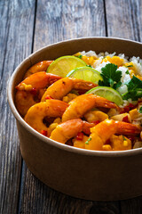 Fried shrimps with rice and vegetable salad in lunch box to go on wooden table
