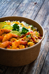 Fried shrimps with rice and vegetable salad in lunch box to go on wooden table
