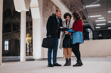 Fototapeta premium Three business coworkers discussing work in an elegantly lit office lobby, with a focus on team collaboration and document analysis.