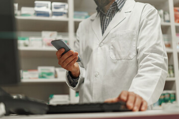 Close up of male pharmacist using the computer and phone while working at the pharmacy