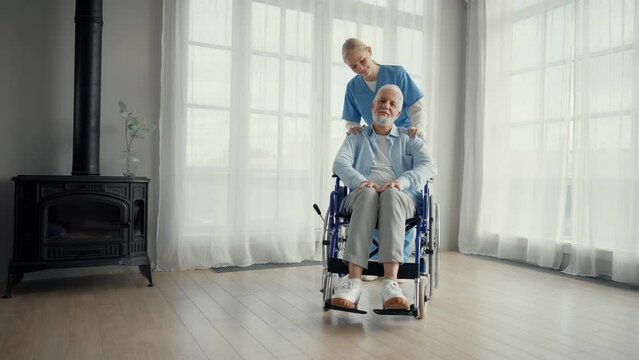 Nurse massaging neck to paralyzed man. Senior male in wheelchair enjoying massage at clinic. Medical worker provides care support help. Living with legs paralysis, special needs patient concept.