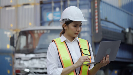  Female engineer in safety uniform uses laptop to control loading of containers from cargo ship for import-export. Logistics, transportation.