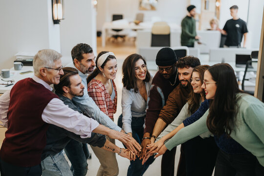 A multiethnic team of colleagues join hands together in a unified show of teamwork and collaboration in a modern office setting.