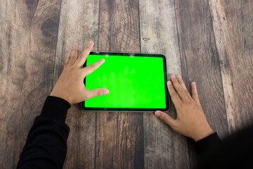 Mock up of a hand holding an iPad tablet with a greenscreen against a wooden texture background