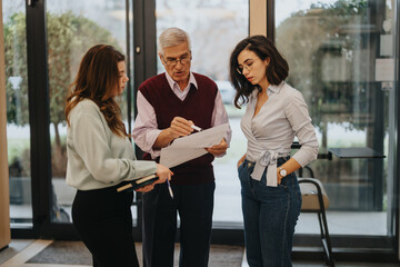 A seasoned business leader reviews paperwork with two professional women in an office environment,...