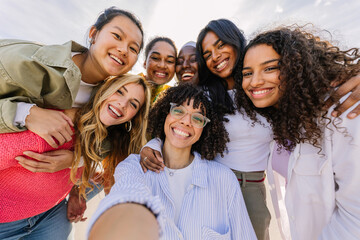 Diverse group of happy young female friends having fun taking selfie portrait together outdoors....