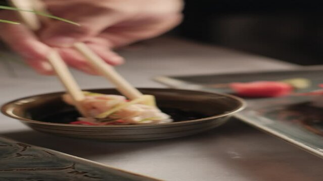 cinematic dripping hand soaking a piece of sushi with chopsticks, in soy sauce with selective focus