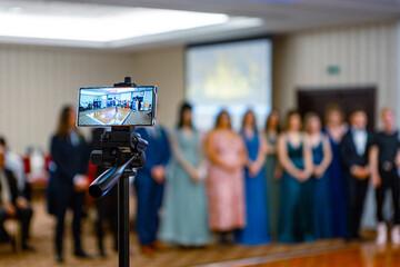 School ceremony being filmed on a smartphone on a tripod