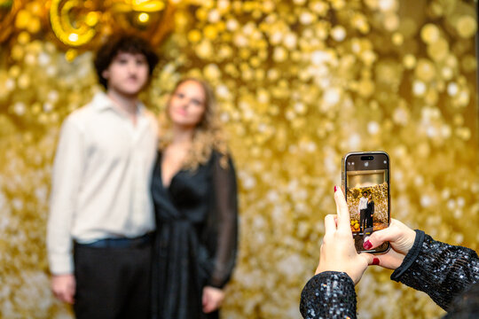 Young couple standing against a golden wall while their mom takes a photo