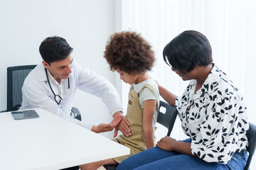 male doctor gently examines a young child's arm with a caring mother looking on in a clinic. Pediatric check-up in progress as a doctor assesses a child's arm with a mother's watchful eye