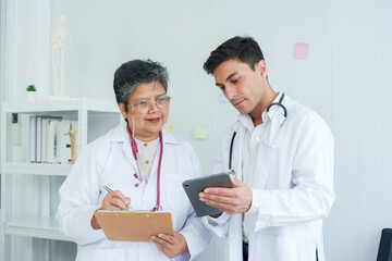 Male and female doctors consult each other with a digital tablet in a bright clinic setting. Two medical professionals discuss patient care using technology in a well-equipped clinic office
