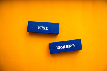 Build resilience lettering on wooden block with orange background. Conceptual symbol. Top view,...