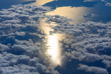 Aerial view of blue sky with white clouds and sun rays over the sea, shot from airplane