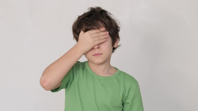 Boy in a green shirt rubbing tired eyes, a sign of fatigue or eye strain. Relevant for health and wellness content about children.