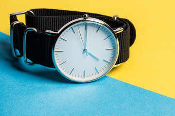 A hand watch with a white shield and tips lying on a yellow-blue background. Photo concept