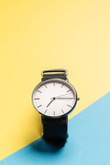 A hand watch with a white shield and tips lying on a yellow-blue background. Photo concept