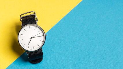 A hand watch with a white shield and tips lying on a yellow-blue background. Photo concept