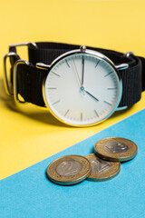 A hand watch with a white shield and tips lying on a yellow-blue background. Next to the Polish coins of PLN. Photo concept