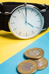 A hand watch with a white shield and tips lying on a yellow-blue background. Next to the Polish coins of PLN. Photo concept