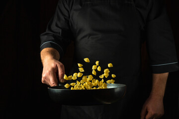 The cook prepares a healthy breakfast of pasta in a frying pan. Healthy vegetarian food and dishes recipe. Place on a dark background for the recipe