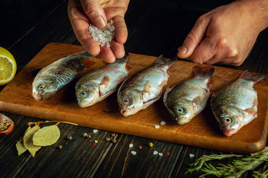 The process of preparing crucian fish on the kitchen table. Chef hands adding coarse salt before drying or cooking Rutilus heckelii