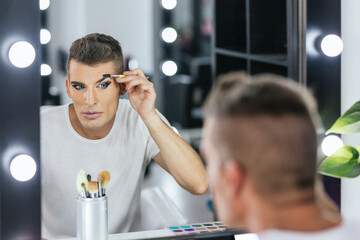Man shaping his eyebrows while doing makeup for a show