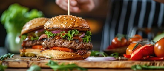 Chef's hand impales juicy hamburgers with a wooden stick in front of meat and veggie-filled table. - obrazy, fototapety, plakaty