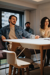 A focused young man in a denim jacket leads a discussion at a modern office meeting, with attentive colleagues surrounding him.