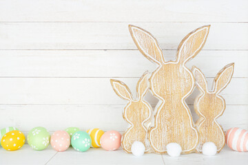 Rustic style Easter decor on a white shelf against a white wood panel background. Wooden bunnies...