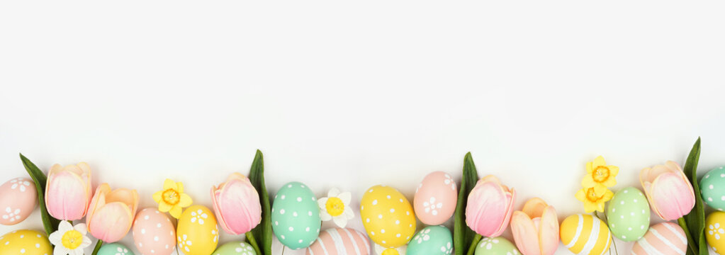 Easter eggs and flower decorations. Top view bottom border against a white banner background. Copy space.