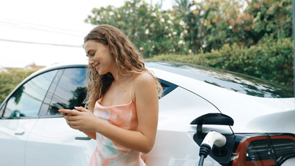 Young woman use smartphone to pay for electricity at public EV car charging station in nature....