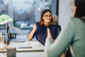 Two women in a business setting are engaged in a collaborative discussion with focus and...