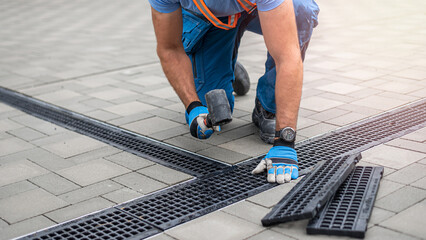 Laying interlocking paving. A worker is placing the grutter grid to drainage channel.