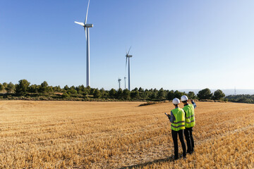 Team of engineers standing in the field inspecting the operation of wind turbines.