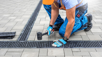Laying interlocking paving. A worker is placing the grutter grid to drainage channel. - obrazy, fototapety, plakaty
