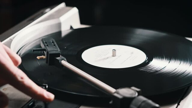 Turntable needle drop on a spinning vinyl record to playing, close up. The vinyl record rotates in the vintage turntable. Stylus rises from vinyl record. Retro-styled old turntable playing retro music