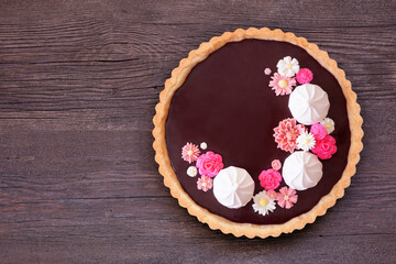 Delicious chocolate tart with meringue and pink chocolate flowers. Above view on a dark wood...