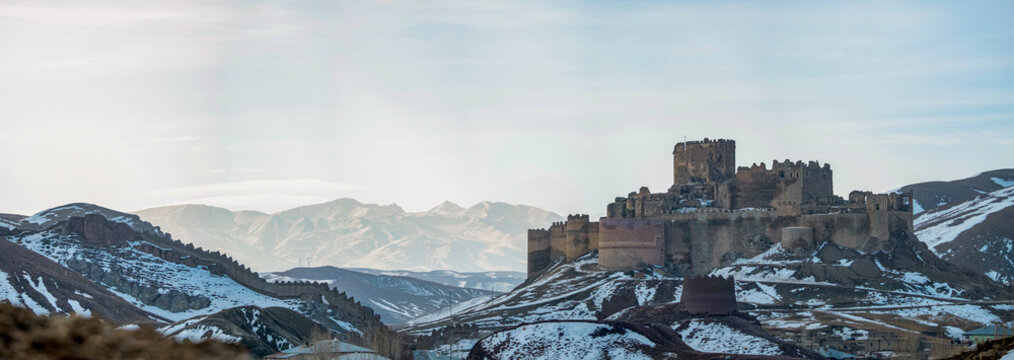 Hosap Castle Majestic Ancient Fortress Nestled in Snowy Mountain Valley. A breathtaking panoramic view of a weathered, ancient fortress, perched atop a snow-covered mountain range. Van, Turkiye