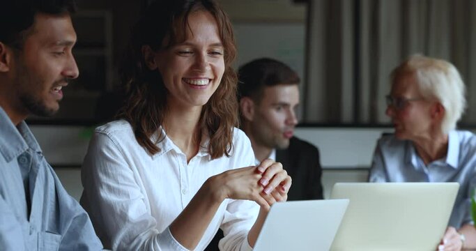 Young multiethnic business colleagues talking at laptop, sitting at meeting table, looking and pointing at screen. Positive Indian mentor man training listening, nodding intern woman at computer