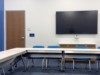 Front of a small meeting room in a public library, with a video camera and wall screen, and a row...