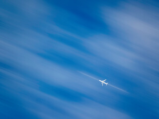 Motion blur of a bright commercial jetliner flying below cirrus clouds on a sunny morning....
