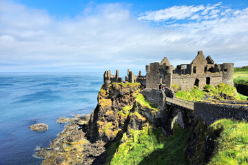 Ruins of the medieval Dunluce Castle on green cliffs overlooking the North Atlantic ocean. Causeway...