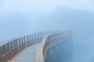 Fototapeta na wymiar Wooden footbridge in a misty waterscape