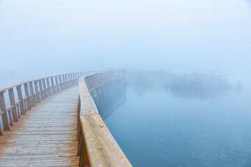 Curving wooden footbridge over a misty lake at dawn