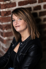 Obraz premium Woman model around thirty in black leather jacket and hot pants in front of urban brick wall.