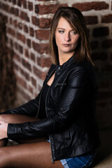 Woman model around thirty in black leather jacket and hot pants in front of urban brick wall.