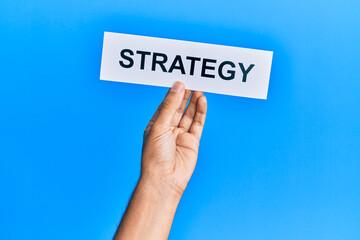 Hand of caucasian man holding paper with strategy word over isolated blue background